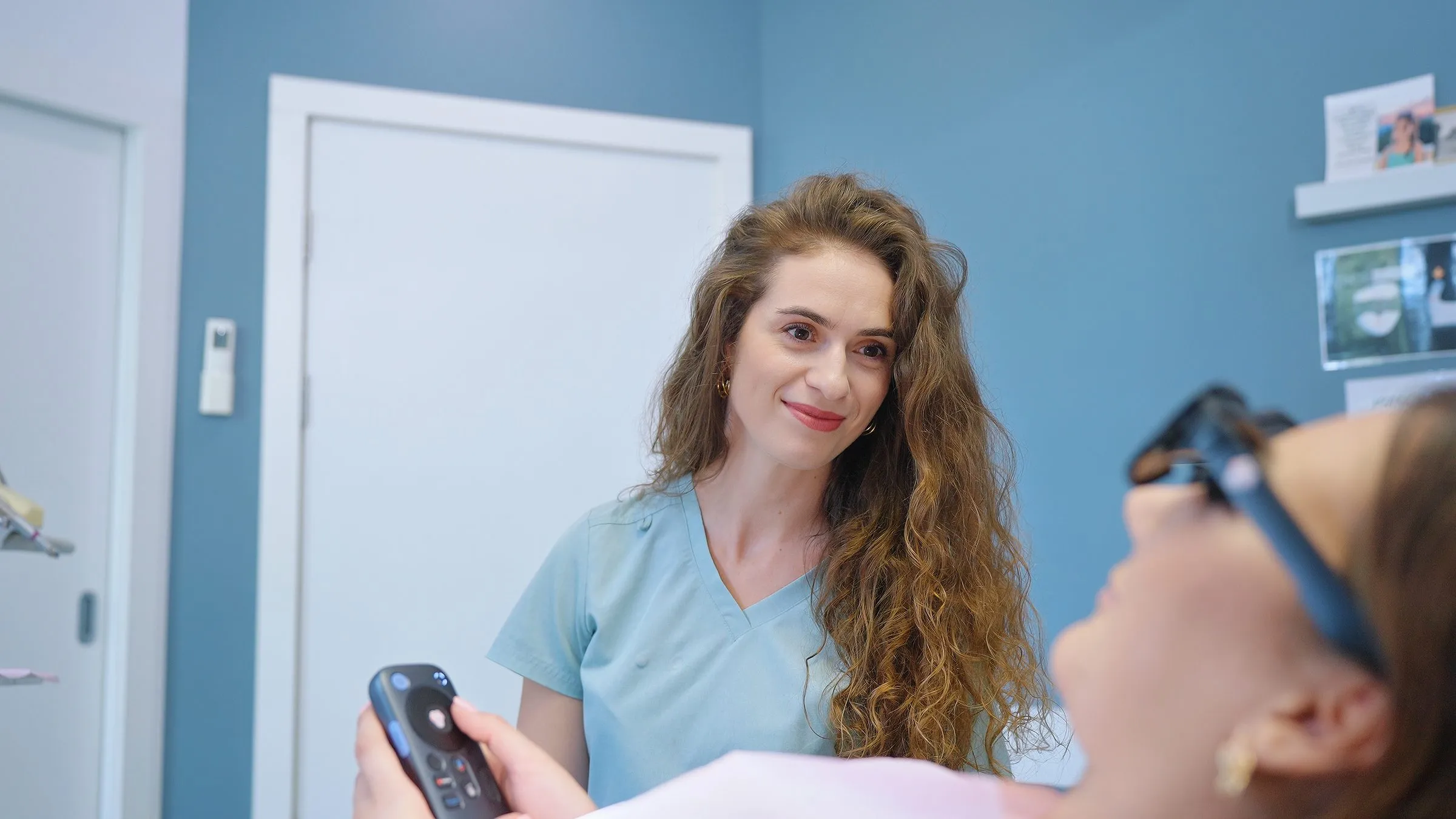 Uśmiechnięta lekarka z pilotem, obok pacjentka w okularach Dental Glasses